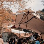 People shopping at outdoor market stalls among autumn leaves