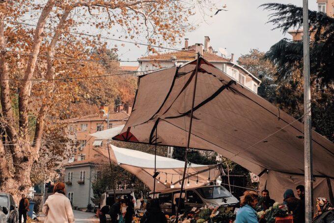 People shopping at outdoor market stalls among autumn leaves