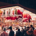 Shoppers browsing a lit Christmas market stall at night