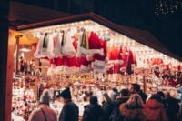 Shoppers browsing a lit Christmas market stall at night