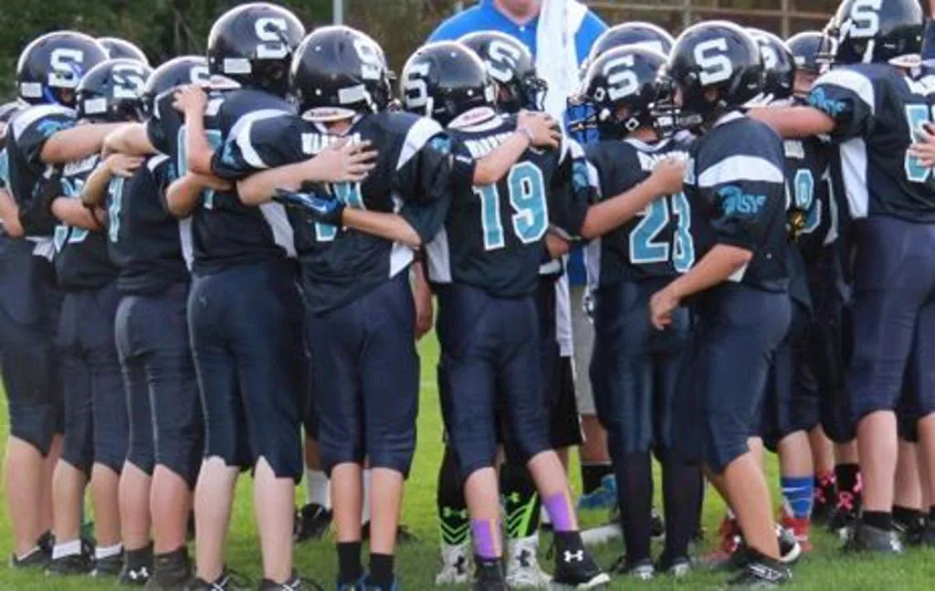 Sparta Spartans youth football players in navy jerseys huddling on the field in Sparta, NJ